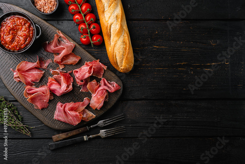 Slices of prosciutto di parma or jamon serrano set, on black wooden background, top view flat lay, with copy space for text photo