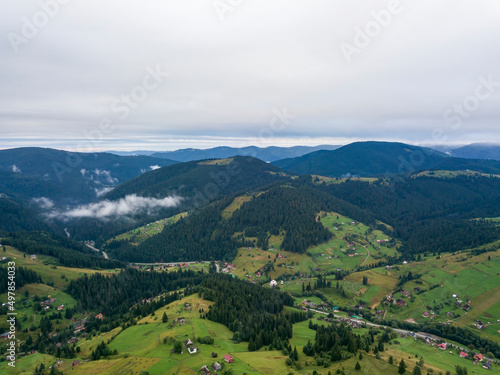 Green slopes of Ukrainian Carpathian mountains in summer. Cloudy morning, low clouds. Aerial drone view.