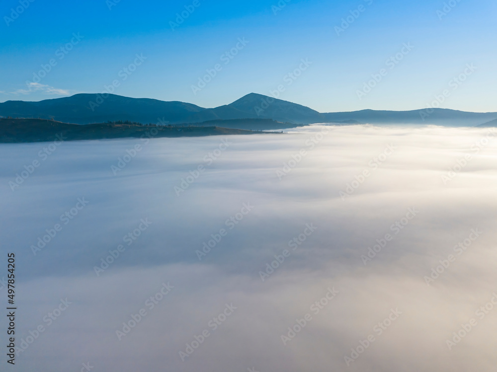 Flight over fog in Ukrainian Carpathians in summer. Mountains on the horizon. A thick layer of fog covers the mountains with a continuous carpet. Aerial drone view. Flight over fog in Ukrainian Carpathians in summer. Mountains on the horizon. A thick layer of fog covers the mountains with a continuous carpet. Aerial drone view.