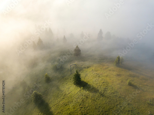 Fog envelops the mountain forest. The rays of the rising sun break through the fog. Aerial drone view.