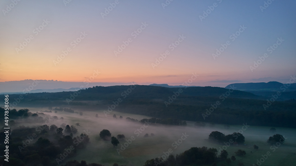 Sunrise in foggy weather. Valley between forests. Hills of the swabian alb in the background. Blue sky for copy space. Aerial view.