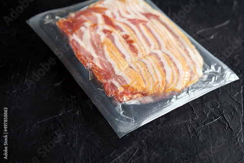 Bacon strips, raw smoked pork meat slices in vacuum package on black table