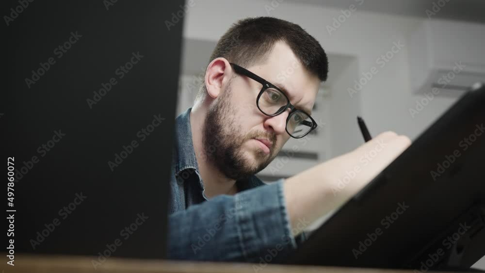 Adult designer in glasses at the workplace. A male freelancer is working on a project with concentration. Adult designer in glasses at the workplace. A male freelancer is working on a project with concentration.