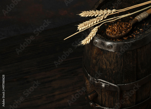 Barley malt for dark beer on a barrel with a spoon and ears of barley, dark background. Ingredient for beer.