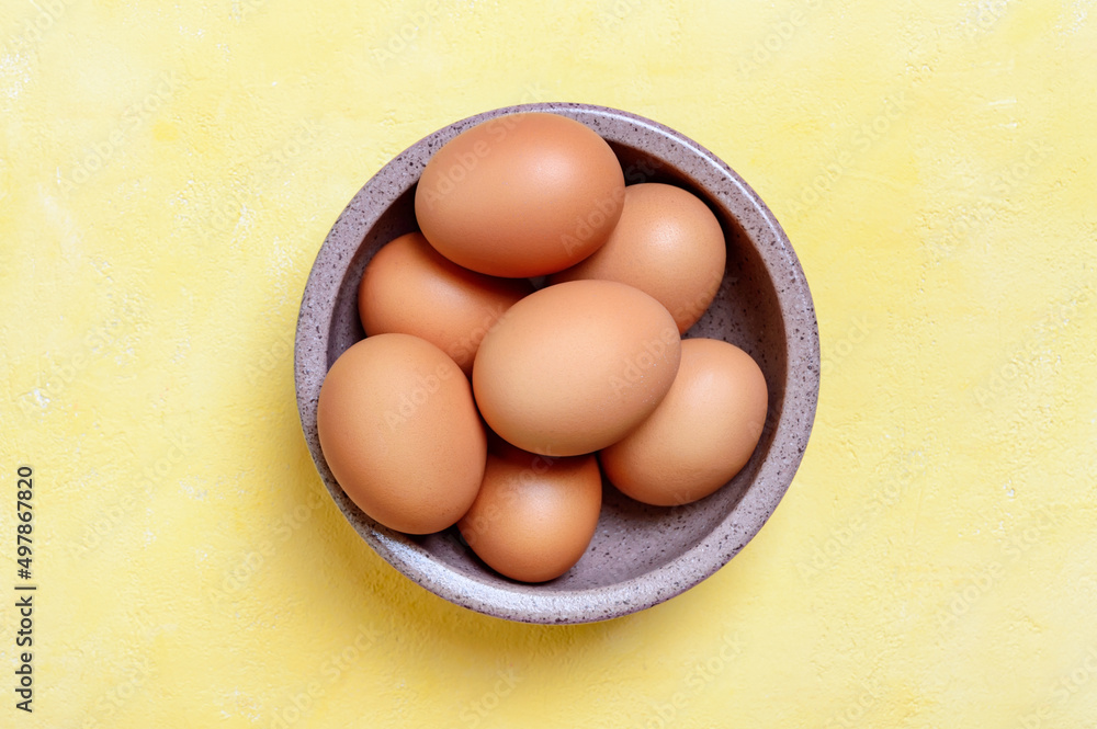 Fresh farm chicken eggs in a bowl on a yellow background. Top view. Fresh farm chicken eggs in a bowl on a yellow background. Top view.