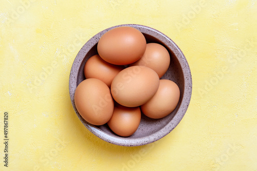 Fresh farm chicken eggs in a bowl on a yellow background. Top view.