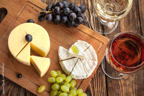 Various types of cheese with dark and green grapes and wine on wooden table.