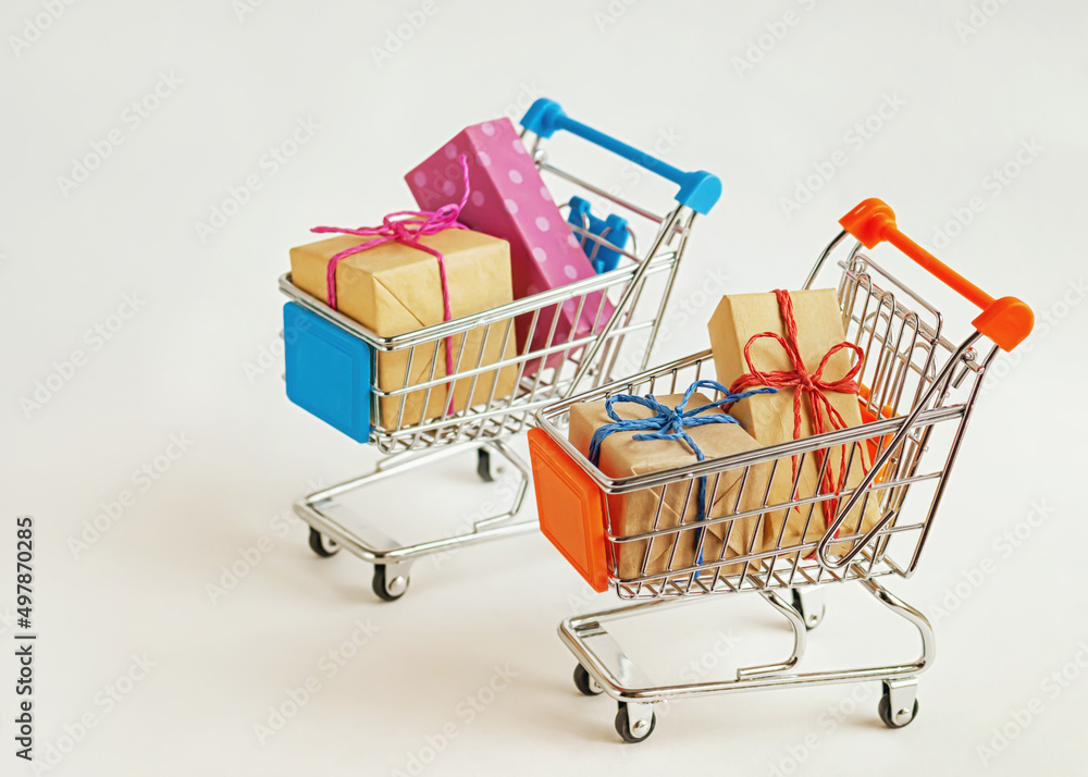 Creative concept of two shopping carts with wrapped gifts on light background, selective focus. Creative concept of two shopping carts with wrapped gifts on light background, selective focus.