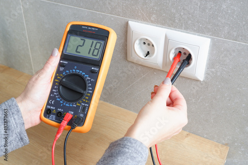 Foto Woman with a multimeter check the voltage of the electrical network