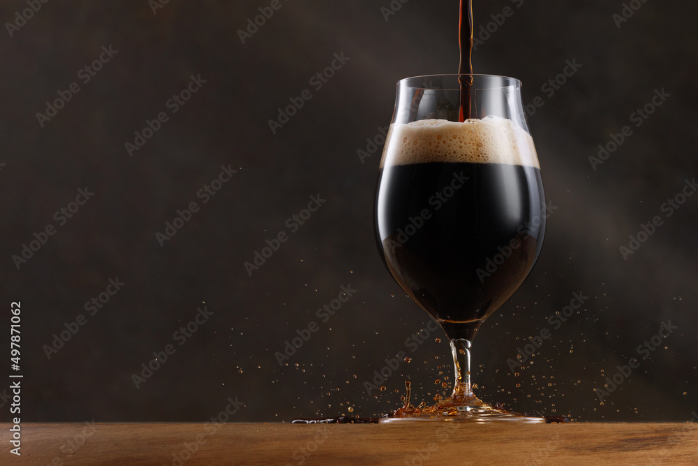 Stream of dark stout pours into a beer glass. Detail of dark beer with overflowing foam head and drips. Selective focus	 - obrazy, fototapety, plakaty 