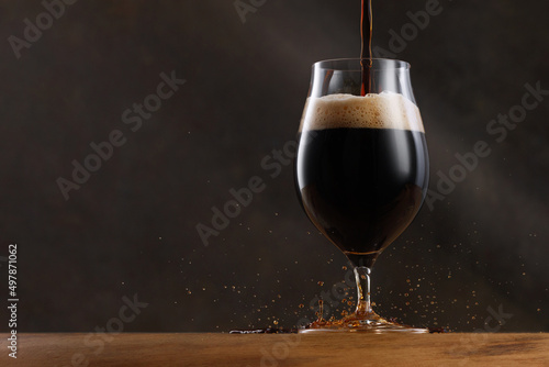 Stream of dark stout pours into a beer glass. Detail of dark beer with overflowing foam head and drips. Selective focus	