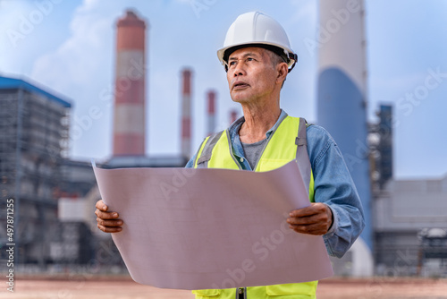 Senior supervisor engineer in his work cloths holding construction blueprints to check on the project progress at the power plant site photo