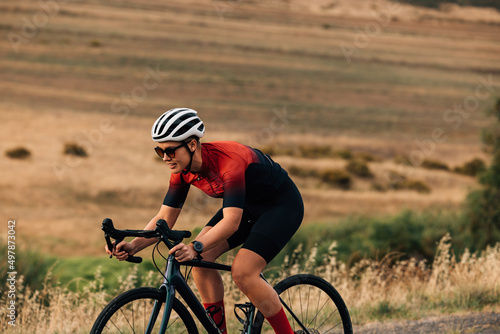 Fototapeta Naklejka Na Ścianę i Meble -  Sportswoman riding a bicycle on a country road. Professional cyclist practicing outdoors.