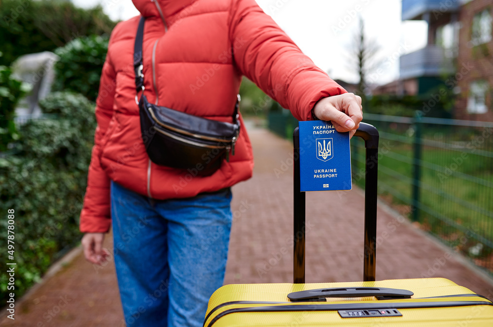 A refugee from Ukraine keeps a close-up of her passport against the background of a suitcase. Refugees and IDPs from Ukraine 2022. Ukrainian symbols. A refugee from Ukraine keeps a close-up of her passport against the background of a suitcase. Refugees and IDPs from Ukraine 2022. Ukrainian symbols.