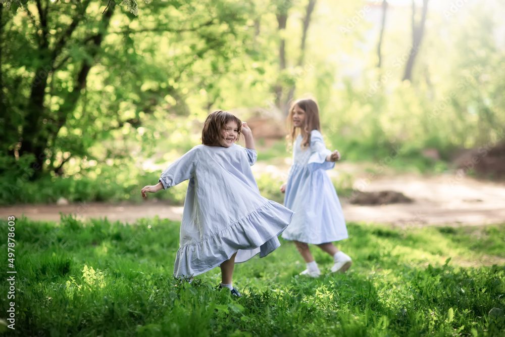 Happy funny children are spinning in the meadow in the park, girls in beautiful dresses hold hands and play in the tall grass. Happy childhood and spring. Happy funny children are spinning in the meadow in the park, girls in beautiful dresses hold hands and play in the tall grass. Happy childhood and spring.