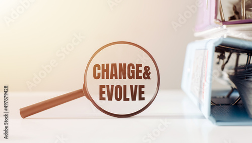 Magnifying glass with text CHANGE AND EVOLVE on white background next to office folders.
