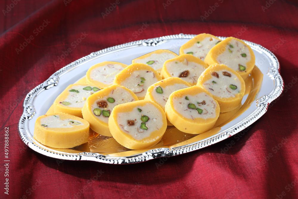 Pedha Indian traditional sweet made of milk served in a silver decorative plate on red silk cloth background Pedha Indian traditional sweet made of milk served in a silver decorative plate on red silk cloth background