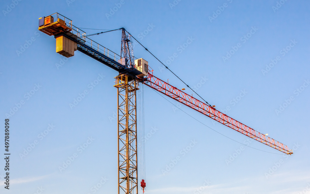 Construction crane. Diagonal view of the crane arm against the evening blue sky. Warm light