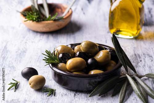 in the foreground a black bowl with mixed olives flavored with rosemary with extra virgin olive oil