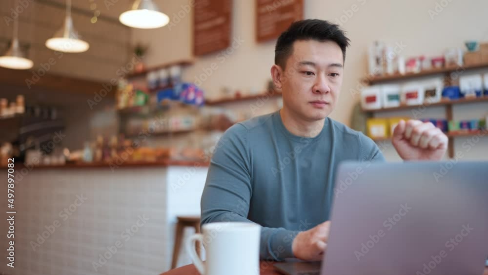 Smiling Asian young man working by laptop and drinking coffee in the cafe Smiling Asian young man working by laptop and drinking coffee in the cafe