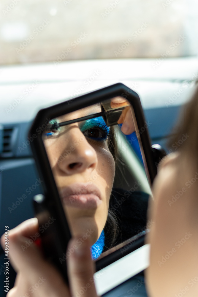 vertical view of a mirror reflection of a woman applying make-up in a car. Eye make up with blue tones