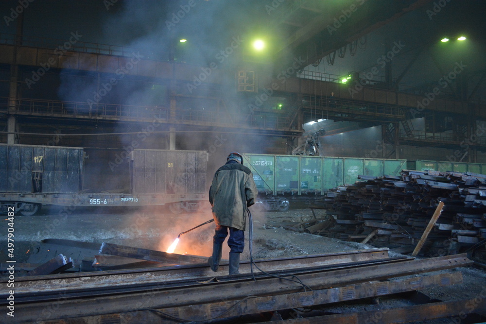 A worker cuts a rail with a gas cutter in the workshop of a metallurgical plant A worker cuts a rail with a gas cutter in the workshop of a metallurgical plant