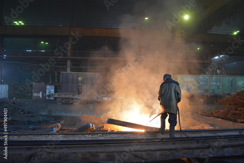 A worker cuts a rail with a gas cutter in the workshop of a metallurgical plant