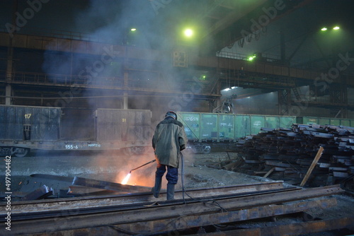 A worker cuts a rail with a gas cutter in the workshop of a metallurgical plant