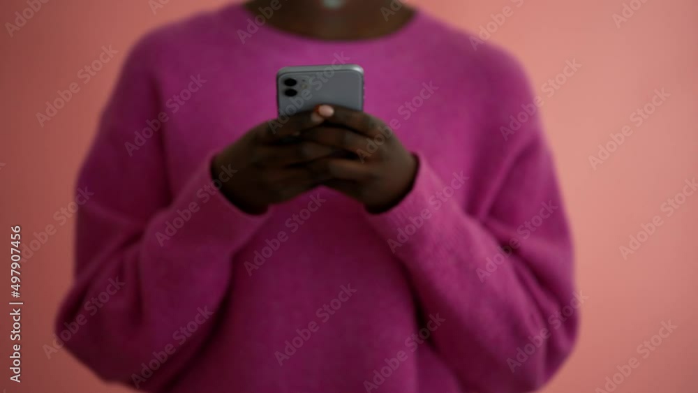 African woman wearing pink sweater texting by phone in the pink studio African woman wearing pink sweater texting by phone in the pink studio