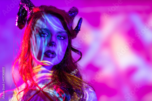 Beautiful young woman with makeup zodiac signs of Capricorn or Aries or Taurus. Girl with horns on head neon light © primipil