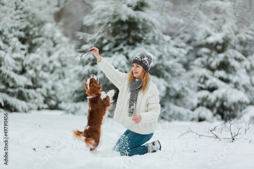 Photography A pretty middle aged woman in yellow hat is playing with her pet dogs in the park in snowy weather