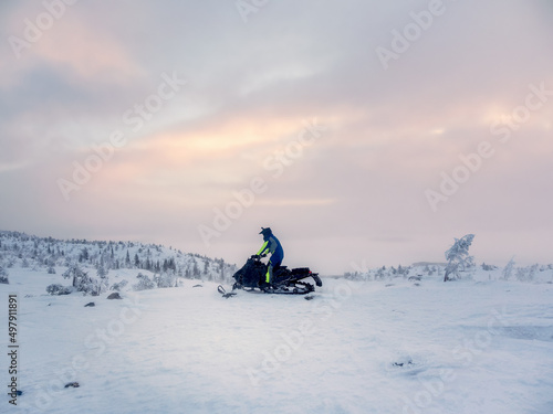 Male on snowmobile in the evening polar hill. Alone man riding up a hill on snowmobile. Extreme winter sports, polar active vacations in the harsh northern nature.