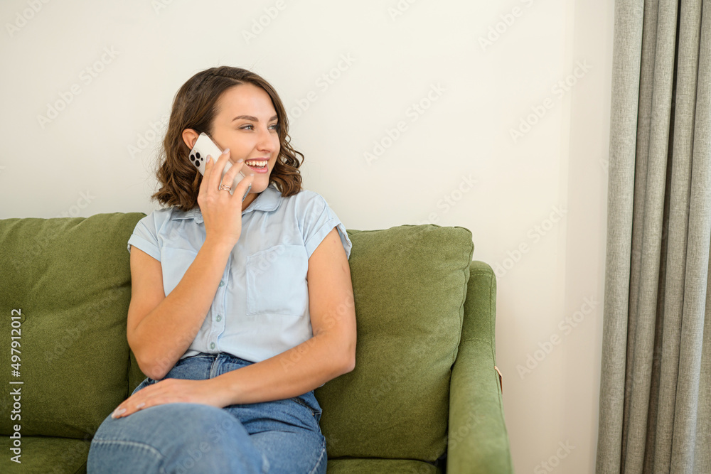 © Vadim Pastuh - Serene young woman talking on the smartphone while sitting on the couch at home, chatting with friends. Attractive female in casual wear sits on the comfortable couch and holding phone conversation © Vadim Pastuh - Serene young woman talking on the smartphone while sitting on the couch at home, chatting with friends. Attractive female in casual wear sits on the comfortable couch and holding phone conversation