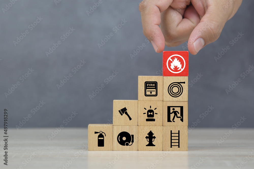 Hand choose wooden block stack with fire prevent icon and door exit sing or fire escape with fire extinguisher and emergency protection symbol for safety and rescue in the building. Hand choose wooden block stack with fire prevent icon and door exit sing or fire escape with fire extinguisher and emergency protection symbol for safety and rescue in the building.