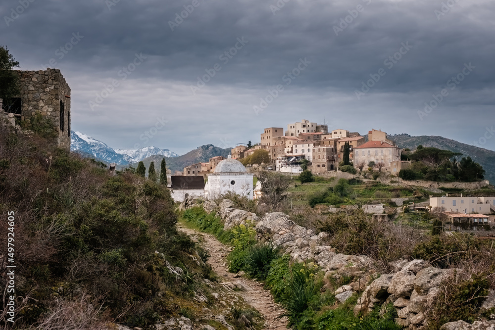 Track leading towards the hilltop village of Sant'Antonino in the Balagne region of Corsica with snow capped mountains in the distance