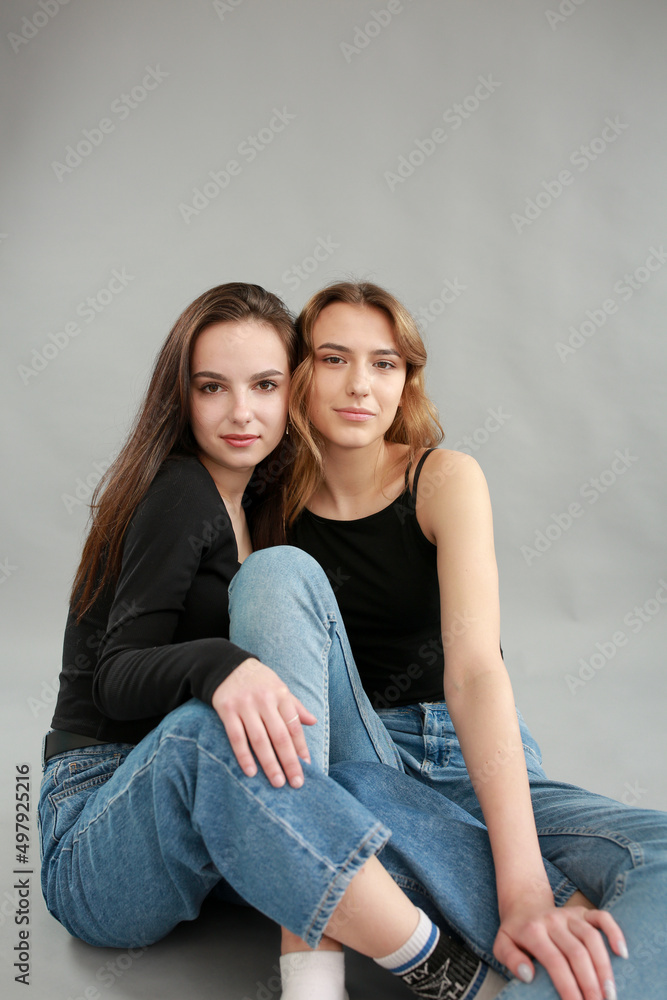 stylish photo shoot of two models blonde and brunette on a gray background in jeans and a black T-shirt. two girlfriends hugging. posing during a photo shoot. young beautiful girls lookbook model stylish photo shoot of two models blonde and brunette on a gray background in jeans and a black T-shirt. two girlfriends hugging. posing during a photo shoot. young beautiful girls lookbook model