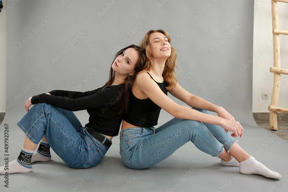 stylish photo shoot of two models blonde and brunette on a gray background in jeans and a black T-shirt. two girlfriends hugging. posing during a photo shoot. young beautiful girls lookbook model stylish photo shoot of two models blonde and brunette on a gray background in jeans and a black T-shirt. two girlfriends hugging. posing during a photo shoot. young beautiful girls lookbook model