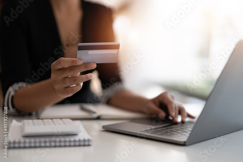 Young woman holding credit card and using laptop computer. Businesswoman working at home. Online shopping, e-commerce, internet banking, spending money, working from home concept © Natee Meepian