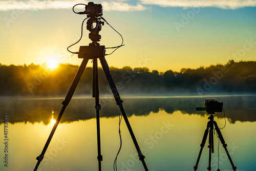 Camera on tripod take photo from sunrise over lake