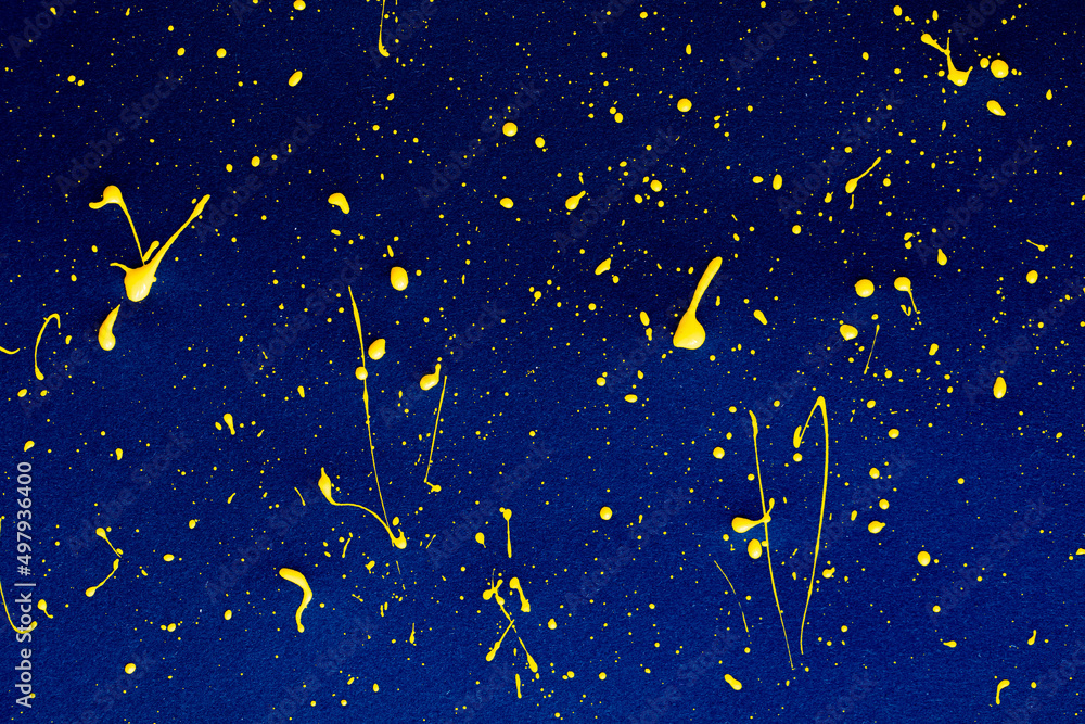 closeup of yellow paint drops on blue paper background