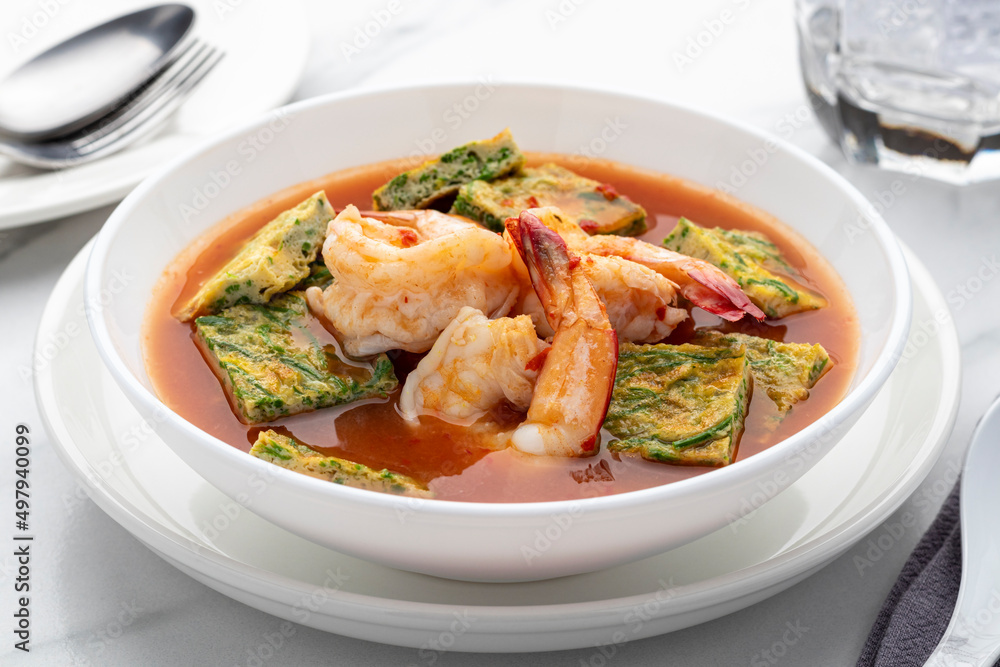 Orange curry, kaeng som in Thai, with shrimps and cha-om omelette served in a white bowl, one of popular Thai food dishes popularly served in restaurants throughout Thailand. 