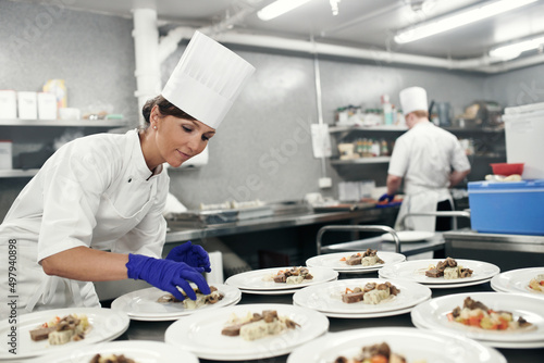 Making dinner into a masterpiece. Shot of a chef plating food for a meal service in a professional kitchen. photo