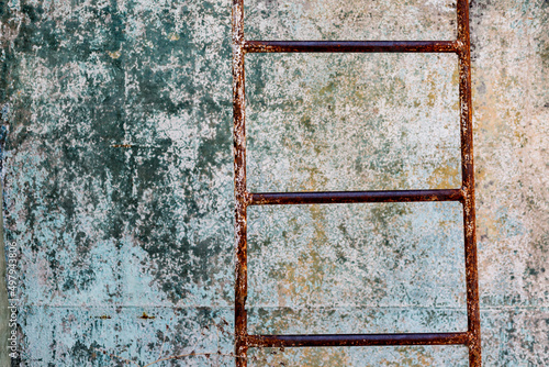 Closeup of rusty corroded metal ladder in abandoned place in front of textured background