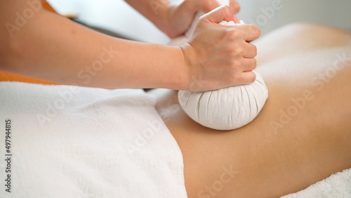 Close up of masseuse hands use hot compress treatment in Thai spa on her back. Woman get a therapy massage for full body. Relaxation from stress of work. Healthy spa and lifestyle concept