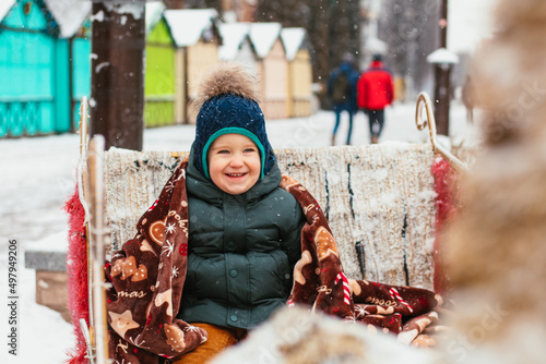 baby boy sincerely smiling without looking at the camera. child on a sleigh with deer. Christmas decorations at the New Year's fair in the city. winter, frost, cold, snow