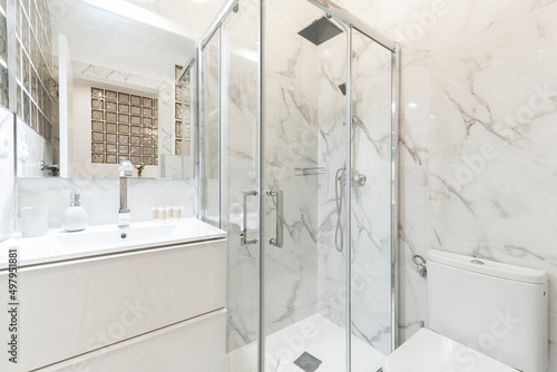 Bathroom with porcelain sink  shower tray  rectangular frameless mirror and walls covered in white marble with gray veins