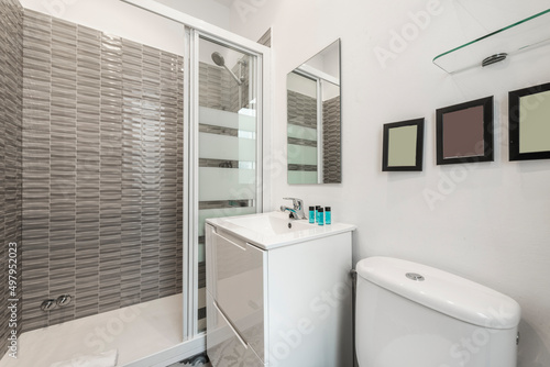 Bathroom with square mirror  white porcelain sink  white lacquered wooden furniture  shower cabin and cork radiator to dry towels