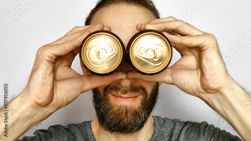 Принти на полотні Close-up of the face of a smiling bearded man putting two beer cans to his eyes