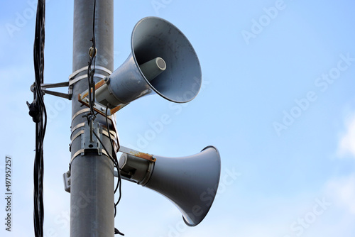 Loudspeakers on pole, alarm siren in city. Two public address system speakers on blue sky background