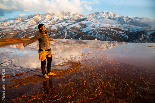 Woman enjoying the sunset at a ferruginous water spring in Iran with snowy mountains in the background. badab-e-surt